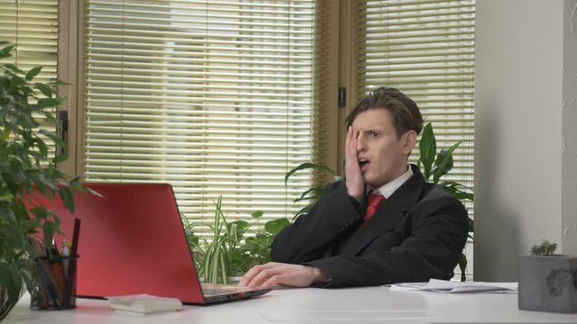 young guy in a suit is sitting in the office, working on a laptop, tired, falling asleep, bored, exhausted. He covers his face with a piece of paper. Work in office. 60 fps