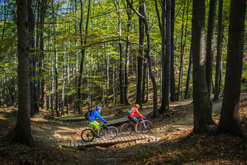 Mountain biking women and man riding on bikes at sunset mountains forest landscape. Couple cycling MTB enduro flow trail track. Outdoor sport activity.
