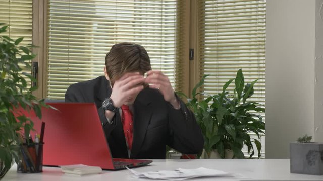Young guy in a suit is sitting at the office, working on a laptop, tired, falling asleep, bored. 60 fps