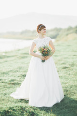Fototapeta na wymiar Bride in wedding dress posing on grass with beautiful landscape background
