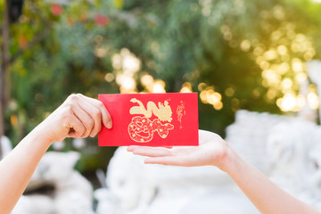 Close up hand holding red letter, sending and receiving red envelope Symbols of the Chinese New Year on golden bokeh background.
