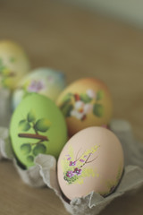 Easter egg hand painted craft decorated. Lying in egg carton. on rustic wood.  Shallow depth of field. Colourful.