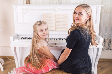 woman teach little girl play piano
