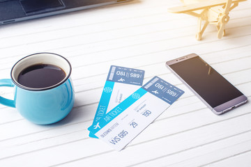 Cup of coffee plane tickets, phone and laptop on white wooden background. Concept of buying the online ticket booking
