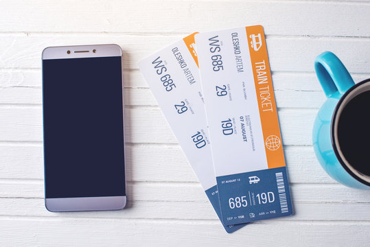 Cup Of Coffee Train Tickets And Phone On White Wooden Background. Concept Of Buying The Online Ticket Booking