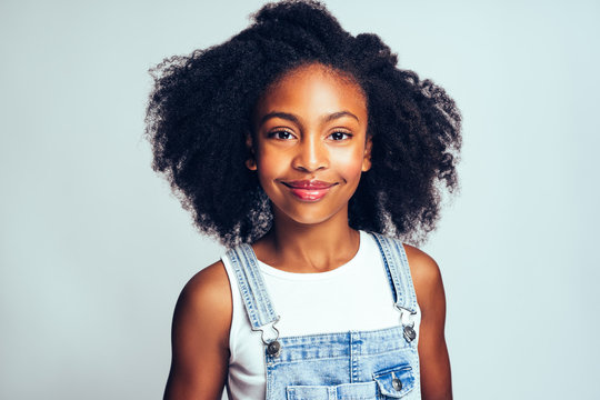 Cute young African girl in dungarees against a gray background