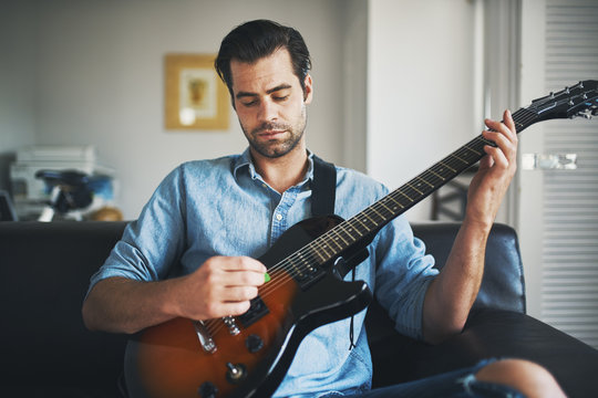 man playing electric guitar on sofa at home