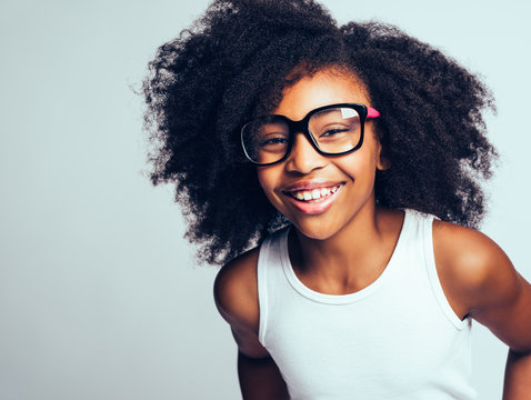 Laughing young African girl wearing glasses against a gray backg