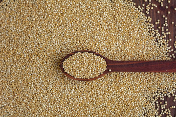 Kinoa seeds in wooden spoon on wooden table, top view
