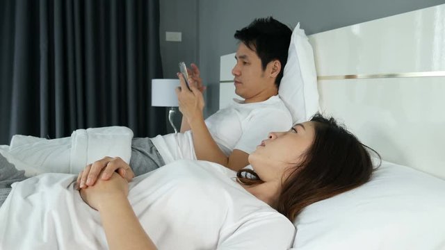 4k of woman having sleepless and her husband texting on smartphone in the bedroom