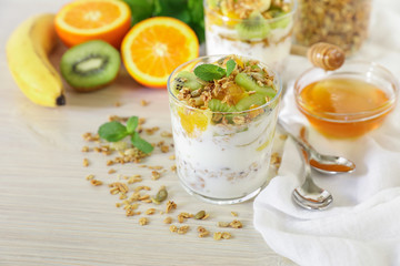 Tasty and healthy breakfast or snack two glasses of yogurt, granola and kiwi, orange, banana slices, honey, mint leaves on a white wooden background.