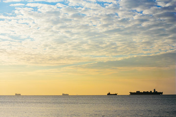 Fototapeta na wymiar Sunny seascape at dawn. Silhouettes of ships on horizon under cloudy morning sky. Beautiful calm sea.