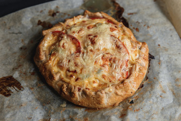 A crispy galette with vegetables and cheese on baking paper on a black baking tray.