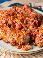 Sausages and pork pullet cooked in traditional Italian tomato ragu sauce. Dish on burlap with cutlery.