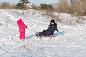 A little daughter and her mother frolic in the snow in a frosty day.
