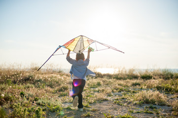 little boy run across the field with a kite in his hands trying to fly