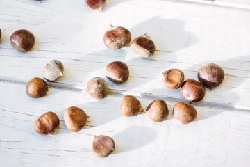 Obraz premium Fresh raw chestnuts on white wooden surface.