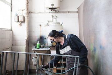 Strong and worthy woman doing hard job. She using industrial spray compressor for painting some metal products.