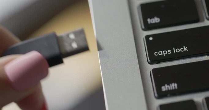 Woman's hand with pink nails attempts to plug in USB cable upside down, then flips it to connect to laptop computer in sunlit interior. Recorded in 4K with dolly move from right to left.