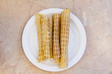 Nice sweet wafer tubes from thin dough lie in row. Tasty baked pastry on ceramic plate