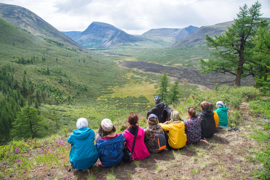 Hikers have a rest on a hillside with beautiful view to the mountains, people relax on summer activity.