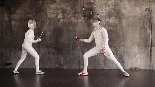 Woman and man are engaging in sporting fencing with rapier. They are learning attacks and protections, preparing for olympic games