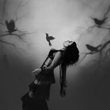 A girl in a black, vintage dress posing against the background of a gloomy forest, which is created by the projector. From her chest bursts the soul, a bird, a symbol of liberation. Play of shadows