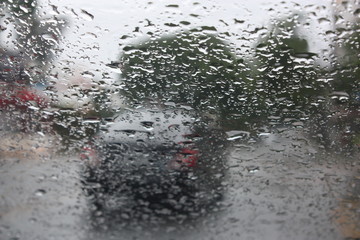 Raindrops on a glass window with blurry trees, road and car