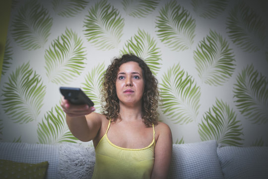Young woman using remote control and watching TV