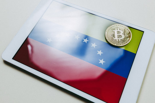 Close up view of a tablet with flag of Venezuela and a bitcoin gold on it