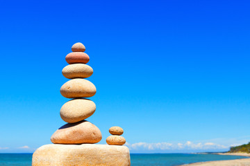 Fototapeta na wymiar Rock zen pyramid of white and pink stones on a background of blue sky and sea.