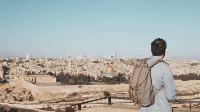 Tourist male takes photos of Jerusalem panorama. Man with backpack stands at skydeck edge with smartphone. Israel 4K.