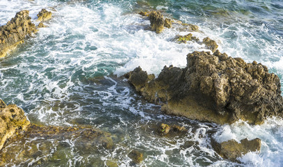 cliff next to the Mediterranean Sea, strong waves break with the rocks and leave blue and turquoise colors along with the foam of the sea.