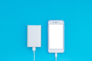White smartphone and charger power bank on a blue background. Top view of the place for the text.