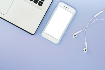 A phone with a white screen, a laptop and headphones on a blue background. Flat Lay gadgets and place for text