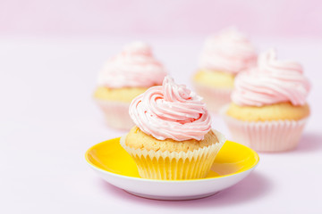 Cupcake decorated with pink buttercream in bright yellow plate on pastel pink background. Sweet beautiful cake. Horizontal banner, greeting card, congratulation. Close up photography. Selective focus