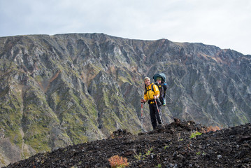 Woman Hiker trekking on mountain top with child in backpack . Summer leisure activity.