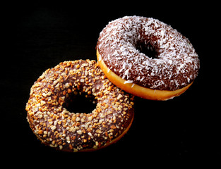 Assorted doughnuts in the glaze, colorful sprinkles and nuts on a black background.