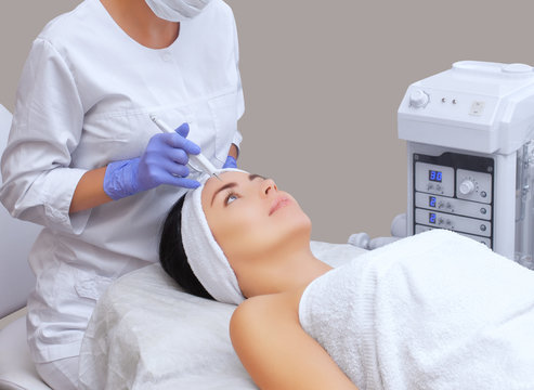 The cosmetologist makes the procedure treatment of Couperose of the facial skin of a beautiful, young woman in a beauty salon.Cosmetology and professional skin care.