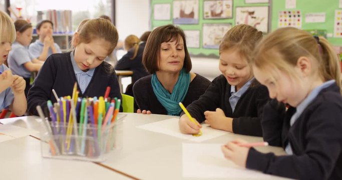 4K Primary school children drawing in the classroom with teacher helping. Slow motion