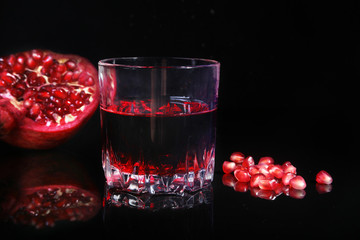 Glass with pomegranate juice Pomegranate seeds and Beautiful ripe pomegranate on black mirror background with place for copy space.