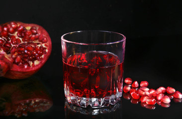 Glass with pomegranate juice Pomegranate seeds and Beautiful ripe pomegranate on black mirror background with place for copy space.