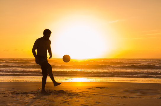 Great concept of soccer, man playing soccer on the beach in golden hour, sunset. Making keepie uppie.