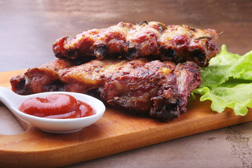 grilled barbecued ribs with lettuce leaves, hot chili pepper and sauce on wooden cutting board.