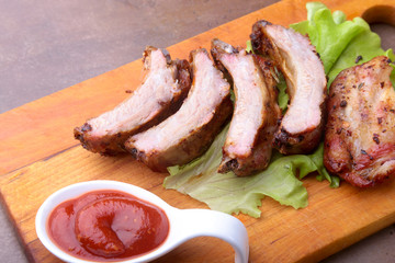 grilled barbecued ribs with lettuce leaves, hot chili pepper and sauce on wooden cutting board.