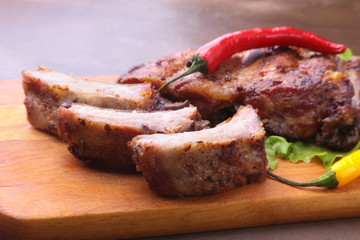 grilled barbecued ribs with lettuce leaves, hot chili pepper and sauce on wooden cutting board.