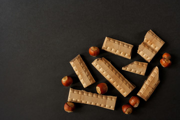 Pieces of milk chocolate and whole hazelnut on a dark background with space for text. Flat lay
