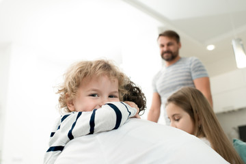 Portrait of adorable little boy smiling happily while hugging mom with the rest of family in background, copy space