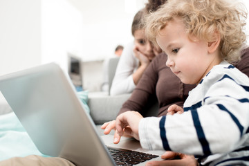 Side view portrait of cute blond toddler using laptop while watching cartoons with mom, copy space