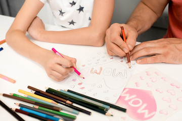 Close up of little girl and her father making holiday greeting cards on Mothers day writing and drawing with pencils